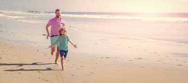 Baba ve oğul yaz plajında açık havada koşuyor. Kopya alanı olan afişler, yaz plajında koşan baba ve oğul. Aile seyahati ve tatil