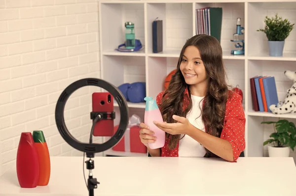 Teenager hold hair conditioner or shampoo bottle recording online media video. Teen girl streaming online and sharing social media content by mobile phone app network