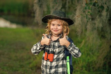 Yaz tatili. Dürbünlü çocuk doğa yürüyüşü yapıyor. Küçük kaşif. Çocuklarla açık hava eğlencesi ve maceralar. Güneşli kırsal kesimde çocuk turist