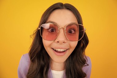 Yüzünde şok ifadesi olan genç bir kız çocuğu. Şaşırmış yüz ifadesi, sarı arka planda izole edilmiş. Mutlu sürpriz.