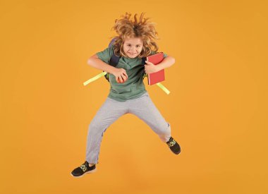Full length of excited kid jumping. School boy in school uniform with backpack jumping on yellow isolated background. Kids learning knowledge and kids education concept