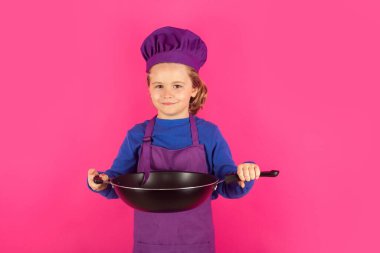 Çocuk tencereyle yemek pişiriyor. Yemek pişiren çocuklar. Aşçı bozuntusu aşçı. Önlüklü ve aşçı şapkalı çocuk mutfakta sağlıklı bir yemek hazırlıyor. Yemek pişirme süreci