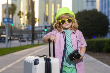 Bavullu mutlu çocuk gezgini portresi. Valiziyle gezmeye hazır küçük bir turist. Bagajı olan mutlu çocuk tatillerde seyahate çıkıyor.