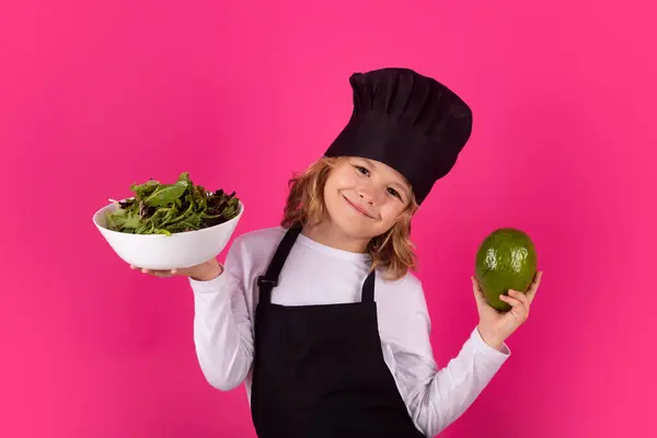 Kid cook with avocado and vegetable. Chef kid boy making healthy food. Portrait of little child in chef hat isolated on studio background. Child chef. Cooking process