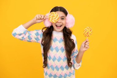 Teen girl hold lollipop caramel on yellow background, candy shop. Teenager with sweets suckers