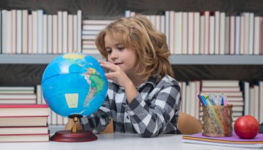 İlkokulun kütüphanesindeki küreye bakan okul öğrencisi. Dünya küresi. İlkokuldan kitaplı çocuk. Eğitim ve öğrenim kavramı