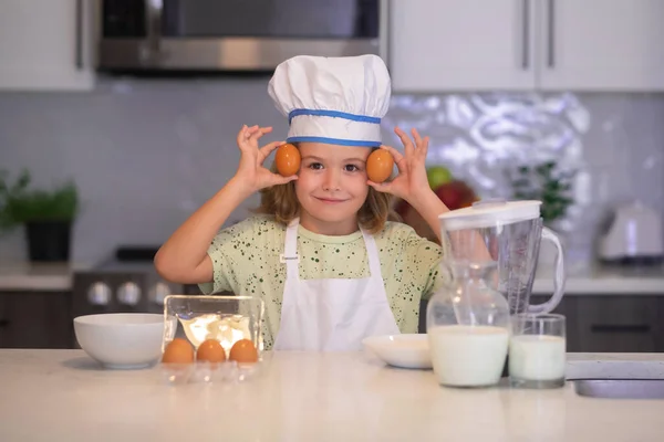 Child chef cook with eggs. Children cooking in the kitchen. Funny kid chef cook cookery at kitchen. Chef kid boy making healthy food. Portrait of little child in chef hat