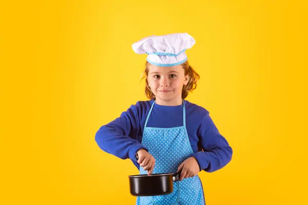 Kid chef cook with cooking pot stockpot. Chef kid boy making healthy food. Portrait of little child in chef hat isolated on studio background. Child chef. Cooking process