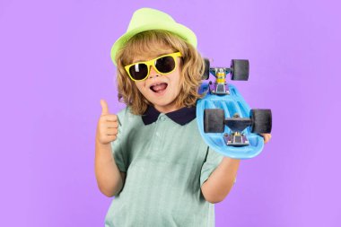Happy child boy holding skateboard over blue background isolated. Studio portrait of fashion kids