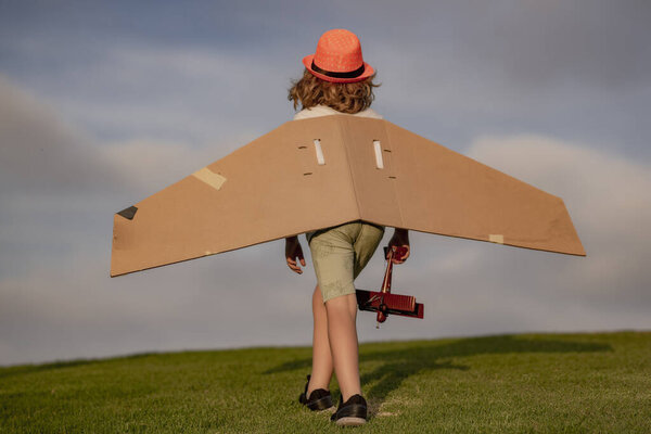 Концепция детского воображения. Счастливый ребенок играет с игрушечными крыльями бумаги на открытом воздухе в летнем поле. Концепция путешествий и детского отдыха. Воображение и свобода