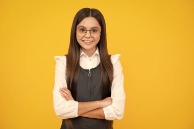 Kollarını kavuşturmuş genç bir kız, kameraya bakıyor, sarı stüdyo arka planında izole edilmiş. Mutlu kız yüzü, pozitif ve gülümseyen duygular