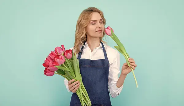 happy flower seller woman in apron with spring tulip flowers on blue background.