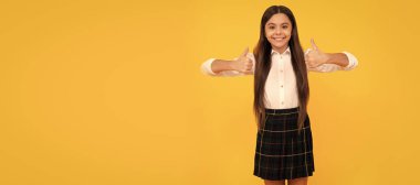 happy child in school uniform full length showing thumbs up on yellow background, positive emotions. Child face, horizontal poster, teenager girl isolated portrait, banner with copy space