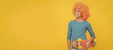 happy teen girl in fancy clown wig hold penny board, childhood. Funny teenager child in wig, party poster. Banner header, copy space