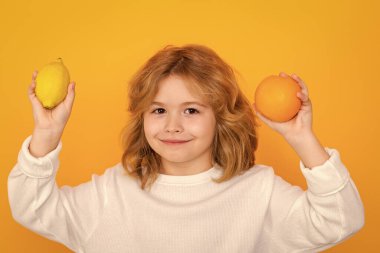 Kid with orange and lemon in studio. Studio portrait of cute child hold lemon and orange isolated on yellow background