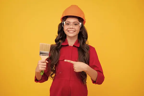 Teenager child painter in helmet with painting brush. Child in hard hat. Kid builder painter on construction site. Renovation and repair. Happy smiling emotions of teenager girl