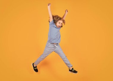 Full length of excited kid jumping. Full length photo of kid boy jump high wear casual checkered shirt isolated on yellow background. Portrait of jumping boy. Kid jumping, having fun