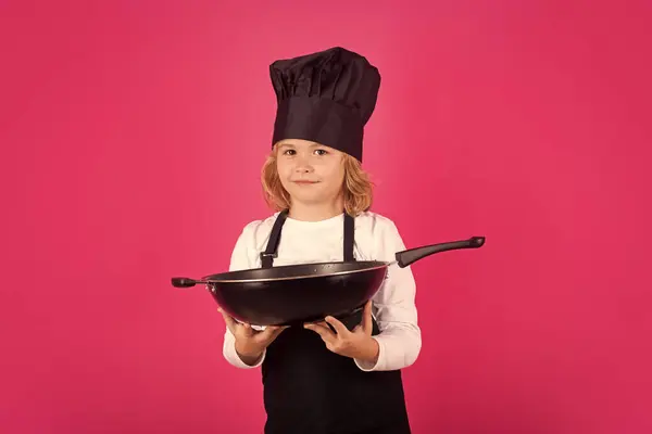 Kid chef cook cookery with pan. Cooking children. Chef kid boy making healthy food. Portrait of little child in chef hat isolated on studio background. Kid chef. Cooking process