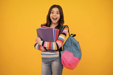 Amazed teenager. School girl hold copybook and book on yellow isolated studio background. School and education concept. Teenager girl in school uniform. Excited teen girl