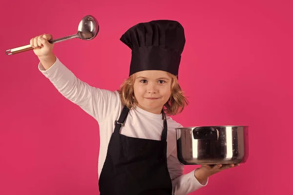 Child chef cook with cooking pot and ladle. Excited chef cook. Child wearing cooker uniform and chef hat preparing food, studio portrait