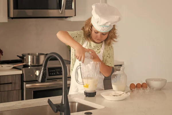 Kid chef cook is learning how to make a cake in the home kitchen. Child making tasty delicious. Eggs, milk and flour ingredients for baking cookies or pancakes