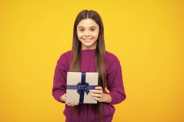 Sarı arka planda izole edilmiş hediye kutusunu tutan genç kız çocuğu. Çocukların doğum günü hediyesi.