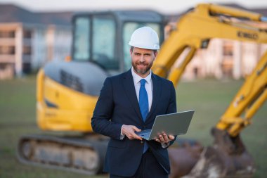 İnşaat mühendisi inşaat alanında çalışıyor. Evin arka planındaki mühendis. Modern ev inşaatında kendine güvenen mühendis. İspanyol inşaat mühendisi miğferinde