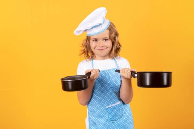 Aşçı çocuk tencereyle yemek pişiriyor. Çocuk fırın üniforması giyiyor ve aşçı şapkası takıyor. Mutfakta yemek hazırlıyor, stüdyo fotoğrafı çekiyor. Aşçılık, aşçılık ve çocuk maması konsepti.