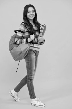 Back to school. Teenager schoolgirl hold book and copybook ready to learn. School children on isolated yellow studio background. Happy teenager, positive and smiling emotions of teen girl