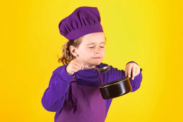 Kid chef cook with cooking pot stockpot. Portrait of little child in uniform of cook. Chef boy isolated on studio background. Cute child to be a chef. Child dressed as a chef hat