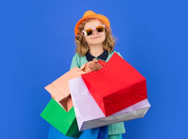 Discounts and sales. Happy Kid boy with shopping bags. Kid with shopping bags posing on blue studio isolated background. Trends and brands