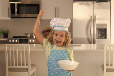Child chef cook with cooking plate. Kid chef cook wearing cooker uniform and chef hat preparing food on kitchen. Cooking, culinary and kids food concept