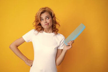 Surprised amazed girl combing hair. Redhead woman with a comb, isolated on yellow background. Women hair care