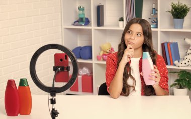 Child vlogger making video blog on phone. Blogging weblog and vlog. Teen girl blogger influencer hold hair conditioner or shampoo bottle recording video for social media.