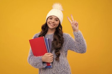Sonbahar şapkalı, sarı arka planda izole edilmiş kitaplarla hayalperest liseli kız portresi. Kış çocuk tatili. Mutlu kız yüzü, pozitif ve gülümseyen duygular