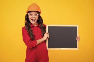 Kask takmış ergen bir çocuk. Kasklı çocuk. Çocuk mühendis inşaat alanında. Yenileme ve onarım. Heyecanlı genç kız fotokopi için tahtayı tutuyor