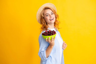 Genç bir kadın tatlı kiraz yiyor. Sarı arka planda kirazlı güzel bir kızın portresi. Yaz meyve toplama mevsimi. Doğal vitaminler