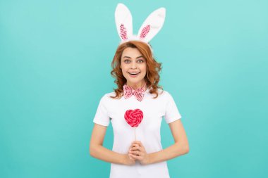 Şaşırmış Paskalya kızı tavşan kulağı takıyor Kalbi tutuyor lolipopu.