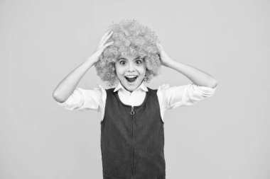 Funny kid in curly redhead wig. Time to have fun. Teen girl with orange hair, being a clown. Excited face, cheerful emotions of teenager girl