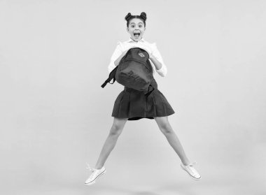 Amazed teenager. Back to school. Teenager schoolgirl in school uniform with backpack. Jump and run. School children on blue isolated studio background. Excited teen girl