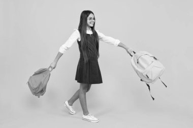 Okul üniformalı okul çantalı kız. Okul çocuğu, genç öğrenci sırt çantasını sarı izole edilmiş arka planda tutuyor. Mutlu kız yüzü, pozitif ve gülümseyen duygular