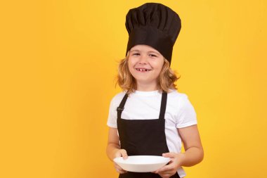 Yemek tabağıyla komik bir çocuk aşçı. Aşçı üniformalı küçük bir çocuğun portresi. Şef çocuk stüdyo arka planında izole edilmiş. Aşçı olmak için sevimli bir çocuk. Aşçı şapkası giymiş bir çocuk.