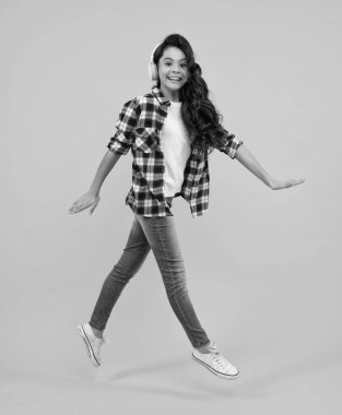 Child music concept. Teenager child girl dances in rhythm of melody, listens song in headphones. Child listening to music through earphones. Happy teenager, positive and smiling emotions of teen girl