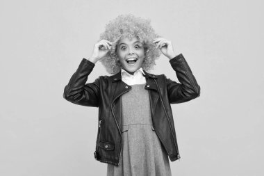 Girl with yellow wig. Funny child wearing orange curly wig hair, summer fun. Excited face, cheerful emotions of teenager girl