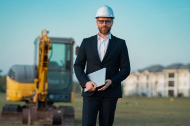 Kazıcının yanında inşaat işçisi. Evin önünde kendine güvenen bir inşaat sahibi. Mimar, inşaat mühendisi. İnşaat alanında güvenlik yeleği ve kasketi olan bir inşaat sahibi.