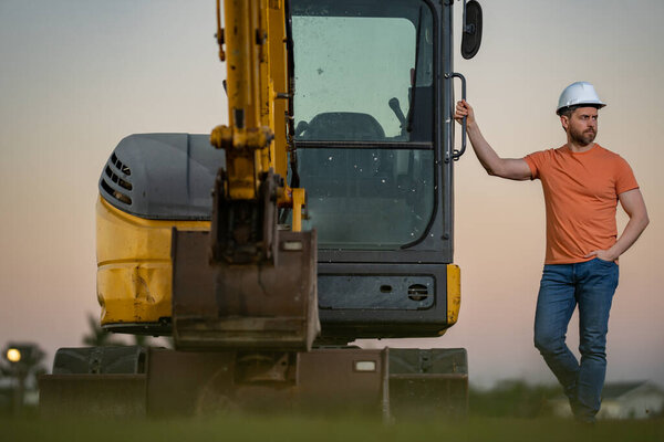 Caucasian man, construction worker in helmet at construction site. Industry engineer worker in hardhat near bulldozer or digger tractor. Concept of construction industry. Construction site manager