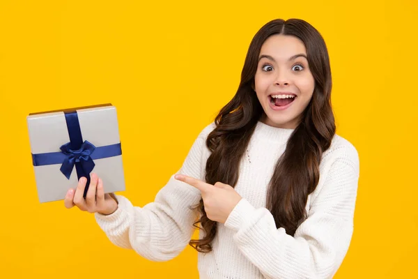 Teenager child holding gift box on yellow isolated background. Gift for kids birthday. Christmas or New Year present box. Excited teenager girl
