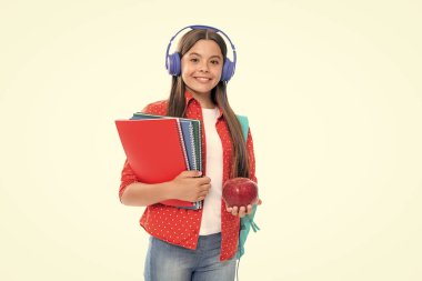 School girl, teenage 12, 13, 14 years old in headphones and books on isolated studio background. School kids with backpack. Portrait of happy smiling teenage child girl