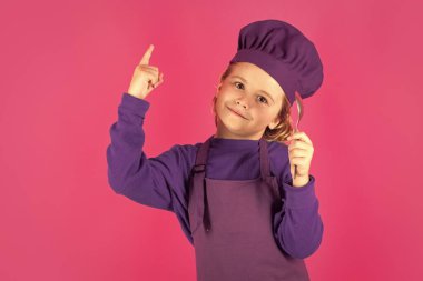 Funny kid chef cook with spoon. Child in cook uniform. Chef kid isolated on pink background. Cute child to be a chef. Child dressed as a chef hat
