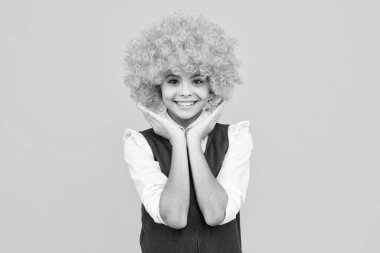 Funny kid with curly hair wig. Cute little girl with fancy hair. Child wearing bright redhead clown hair wig. Happy girl face, positive and smiling emotions